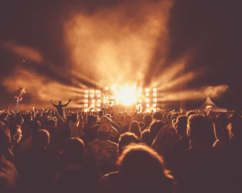 Crowd of fans with hands raised under stage lights at a concert