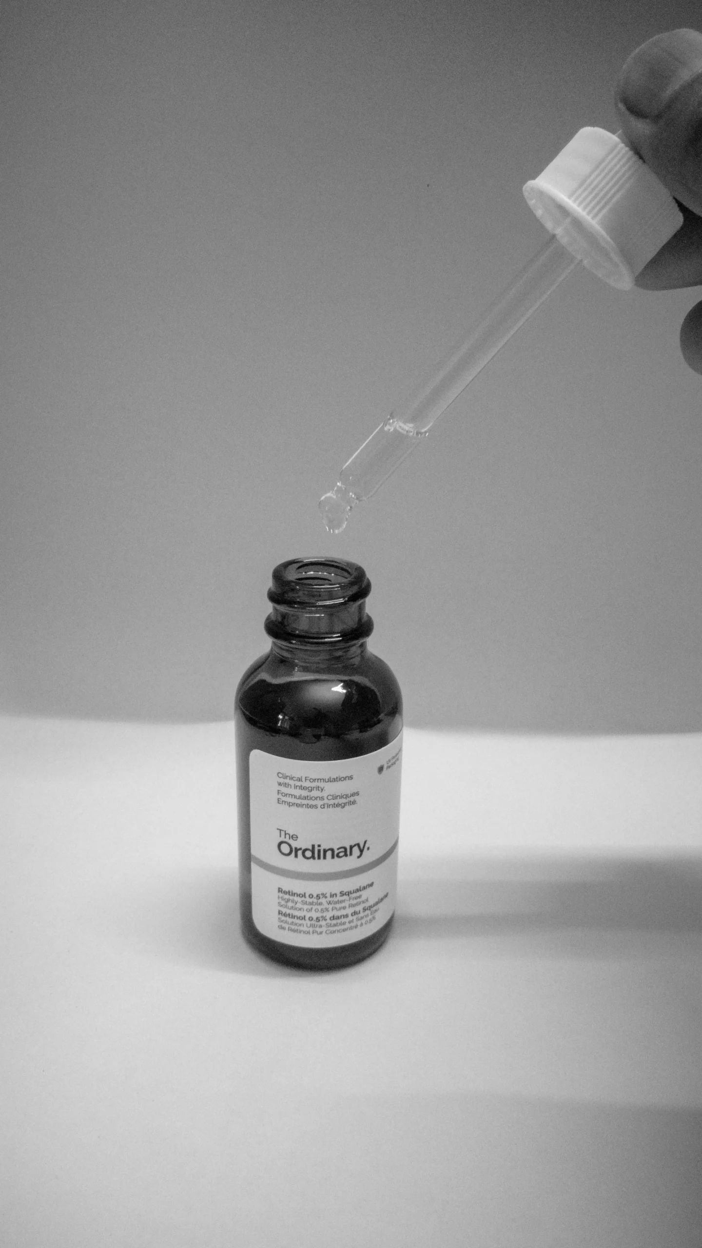 Hand holding a serum dropper over a skincare bottle