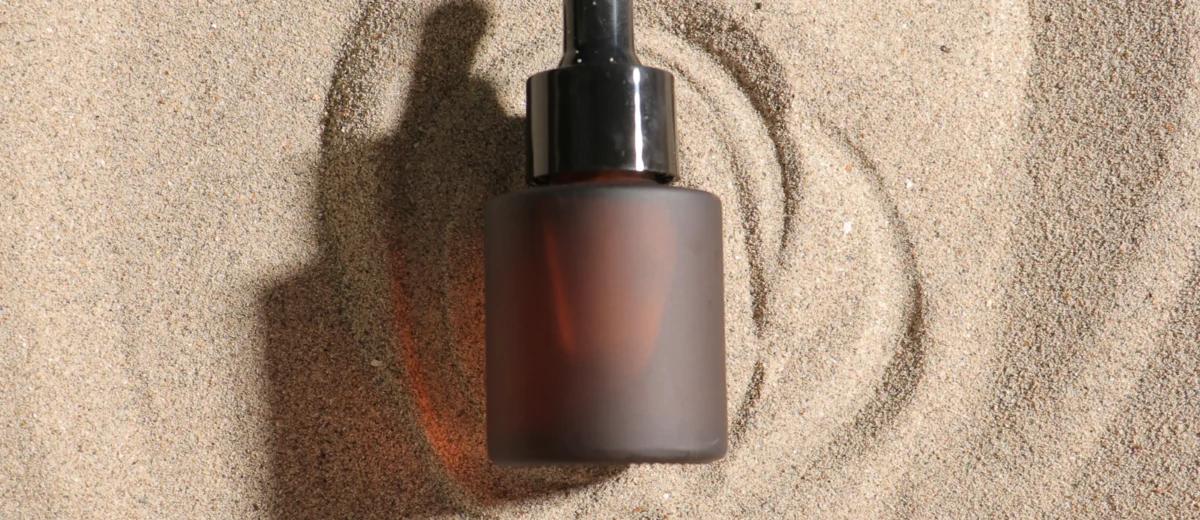 Minimalist frosted glass serum dropper bottle on sand