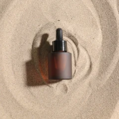 Minimalist frosted glass serum dropper bottle on sand