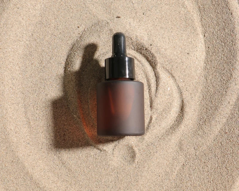 Minimalist frosted glass serum dropper bottle on sand
