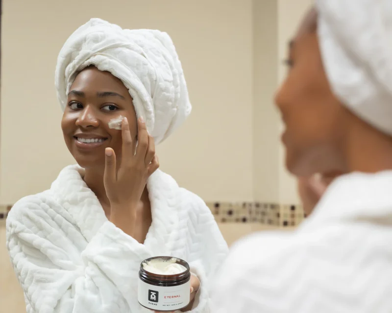 Woman with a towel on her head holding a jar of face cream